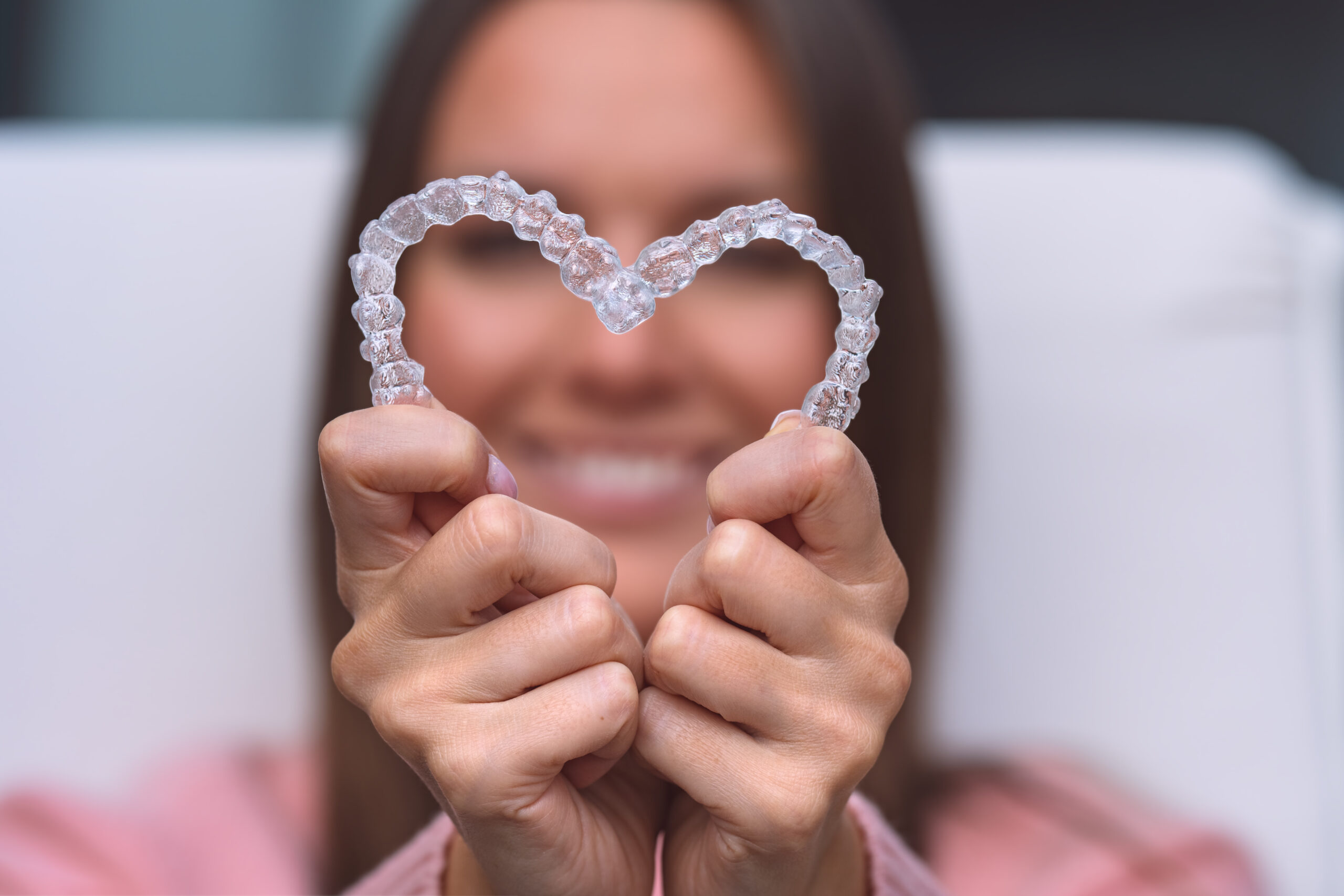 Woman holding Invisalign clear aligner shaped like a heart for cosmetic teeth straightening