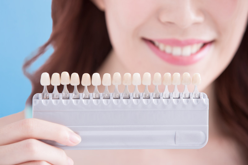 Woman holding veneer shade guide to choose natural tooth color in cosmetic dentistry