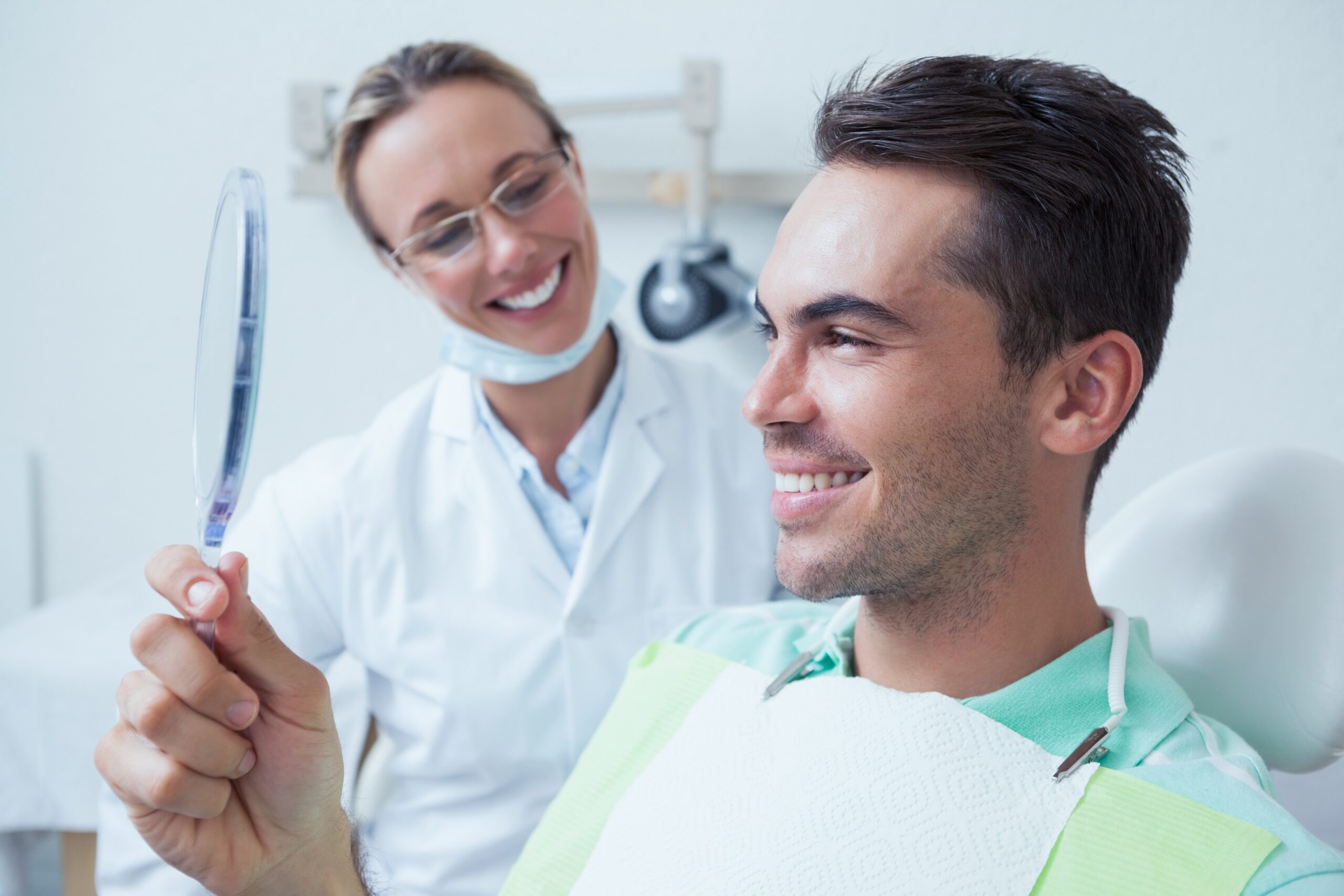 Man smiling and checking his healthy gums in a handheld mirror after periodontal treatment at Plainsboro Dental Services in Plainsboro, NJ.